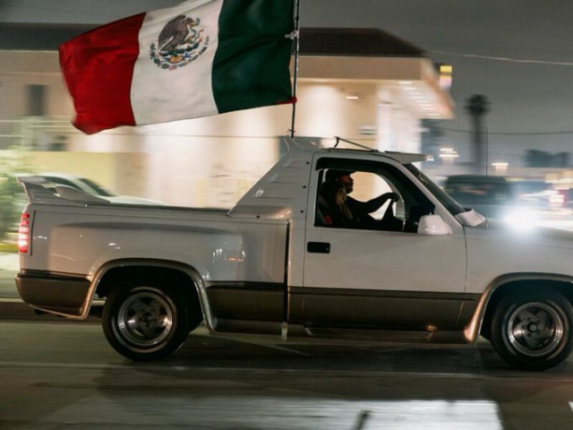 Picture of a white pickup truck flying a huge Mexican flag