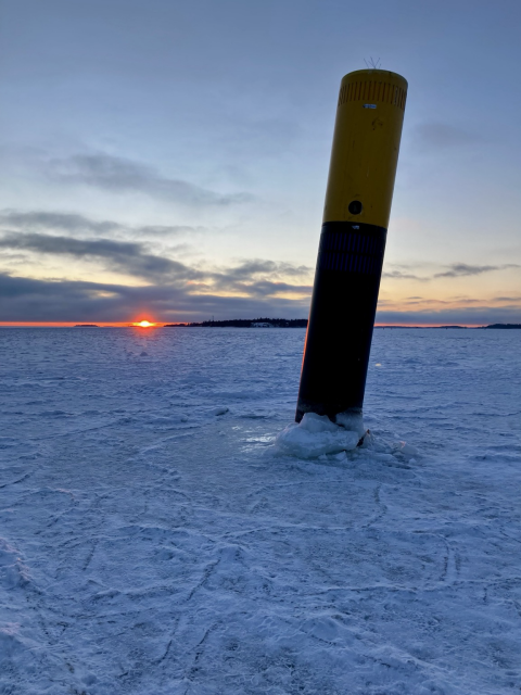 Jään ympäröimä merimerkki. Taustalla horisontissa punainen auringonlasku ja pieniä saaria