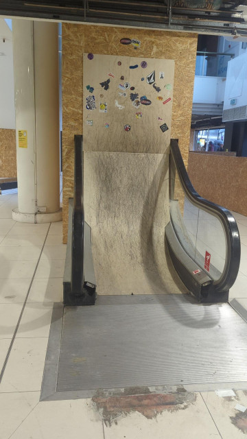 Photo of the start to an escalator including the black handrails. The steps replaced with a skate ramp.