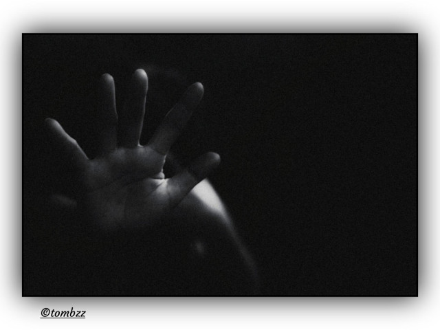 A raised hand held in half‑shadow, fingers slightly spread, suspended between reaching and shielding. Side light reveals the texture of the skin and the fine lines while the background remains completely black. The tension comes from the contrast between the illuminated surface and the surrounding darkness. An analog black and white photograph, raw and focused on a gesture whose meaning stays unresolved, as if the frame captured a moment before intention becomes clear.