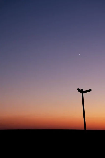 Wolkenloser Himmel mit Sonnenuntergangsfarben. Rechts eine Wegweiser Silhouette. Ein Stern am Himmel.
Hochformat.