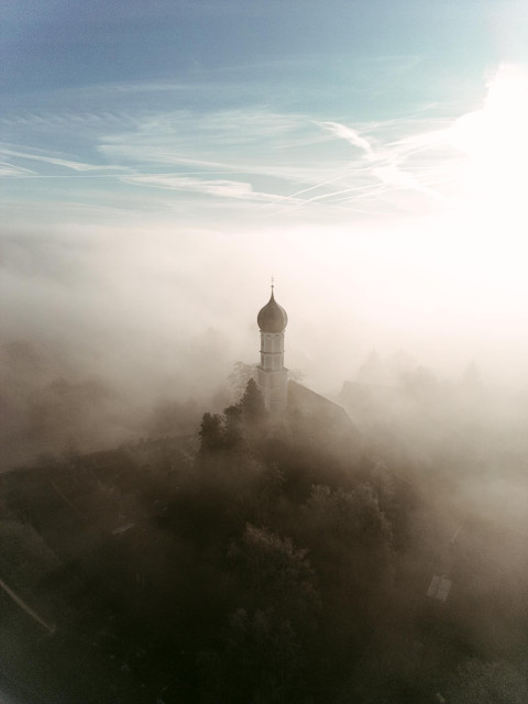 Drone shot of an old church in rural Bavaria peaking through a thick layer of fog