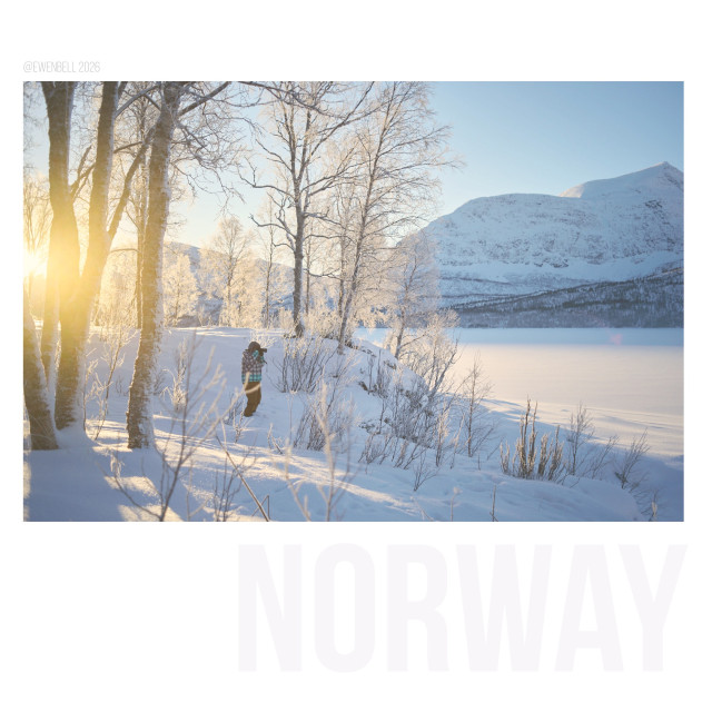 John is standing amongst the birch trees with the sun shining into the lens, taking photos across the frozen lake with views to the distant mountain peaks.