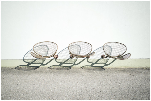 3 Drahtgeflechtstühle die vor einer hellen Wand schweben und einen Schatten werfen