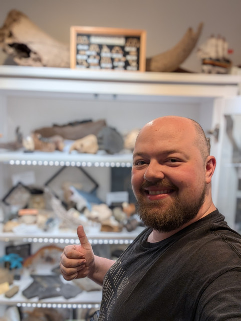 Porträt von mir, Malte Aurich alias MaltastikFed vor einem nicht im Fokus befindlichen Teil meiner Fossilien-Sammlung.