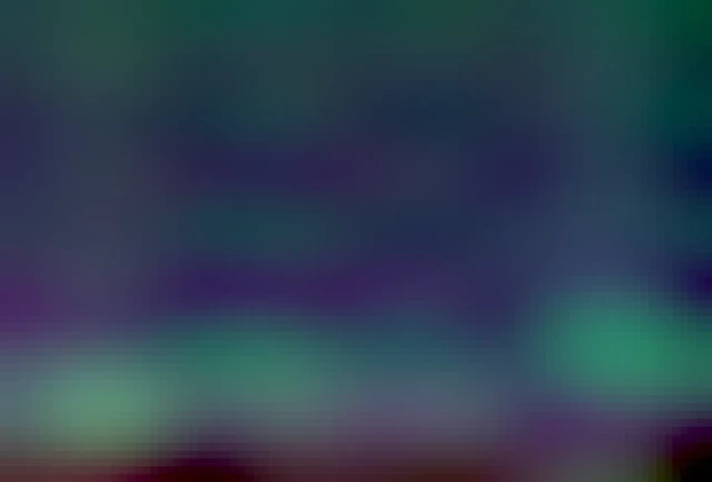 A starry sky with a tree line at the bottom of the image. Some lights from street lights and houses between the trees. Above, a green bow of Aurora borealis is dancing across the sky with some great pilars which are turning in tho red half way up in the sky at both the right and left side. 