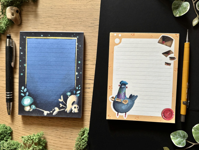 Picture of two different notepads on a black and wooden background framed with decorative plants. 
The notepad on the left is dark blue with funky skulls in the bottom right corner, a few bones, and some glowing plants. 
The notepad on the left is framed with yellow with a white center. On the bottom left is drawn a mailman pigeon, on the bottom right is a wax stamp, and on the top right a few flying letters.