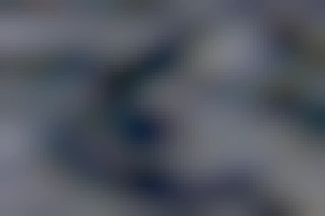 Drifting snow on the frozen sea where the ice has created vertical wavy lines with cracks from the waves. The low sun creates blue shadows behind the cracks and prevents the wind from blowing some of the snow away. Overall, it creates an abstract pattern of vertical, curvy lines and patches of abstract patterns upon the dark ice.