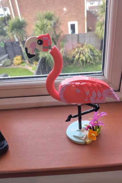 A Lego flamingo stands, on one leg, on the windowsill of my office