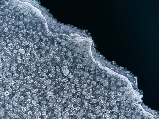 Is på en sjö sett uppifrån. Till vänster i bilden  är äldre is som har frusit i många små cirklar. Till höger i bilden är ny, tunnare is som är helt transparent och det enda som syns är det mörka vattnet. Övergången mellan de två isarna delar bilden diagonalt.