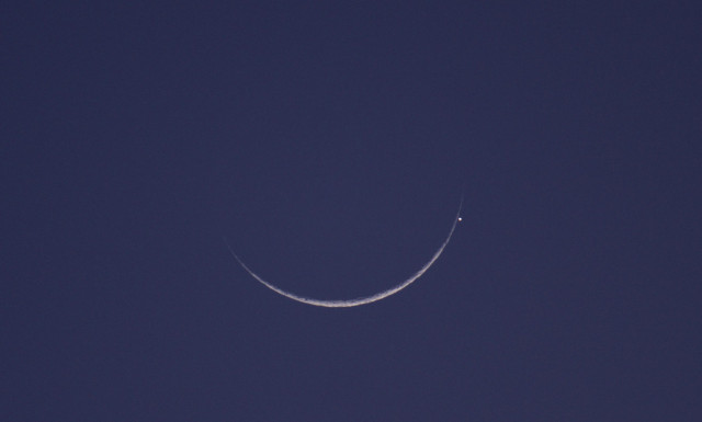 The twilight sky is a medium blue while the crescent moon is a bright gray. Mercury is the overexposed white dot near the left horn of the crescent moon. Some crater and terrain detail is visible on the moon. Twilight is still so bright that we can't yet see earthshine on the rest of the moon's disk. 