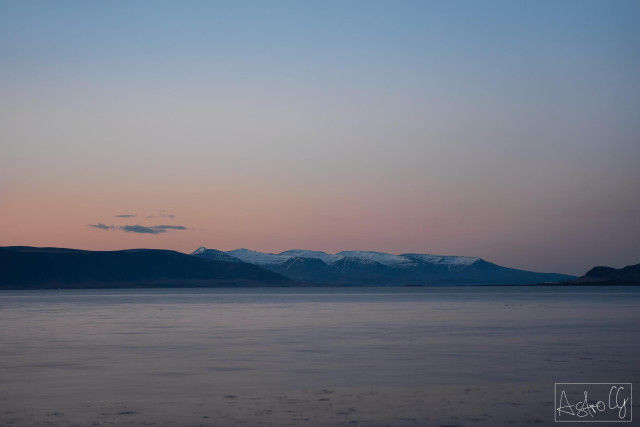 Mountain range with snow-covered peaks under a clear sky above calm water
