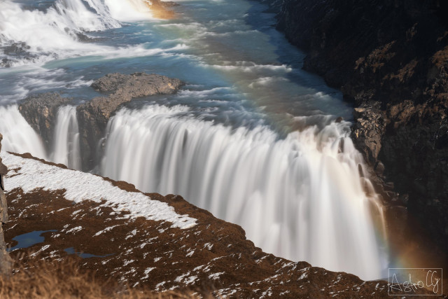 Waterfall with strong flow and rainbow over rocky terrain
