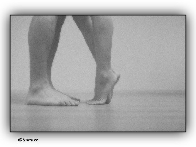 A black and white photograph showing the lower legs and feet of two people standing face to face. It’s me and my wife, captured in a quiet, intimate moment. Her feet are lifted onto her toes, as if she’s trying to close the distance, reach me, step even deeper into this shared moment. My feet rest firmly on the ground, creating a contrast between steadiness and lightness. The frame is simple yet filled with tension and tenderness. From this perspective you can see our small world built on subtle gestures that speak louder than words. It’s a look at feelings from a different angle, at all those moments that need to be lived attentively, felt fully and appreciated before they slip away.