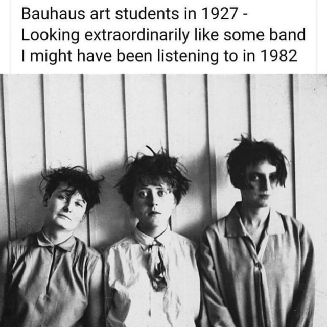 A black-and-white internet meme featuring a vintage photograph of three young women.

Above the photo, the text reads: "Bauhaus art students in 1927 - Looking extraordinarily like some band I might have been listening to in 1982".

The three women in the image have short, messy, avant-garde haircuts and are wearing collared shirts or blouses. They are standing side-by-side against a wall with vertical panels, looking at the camera with serious, deadpan expressions that strongly resemble the moody aesthetic of a 1980s post-punk or new wave band.
