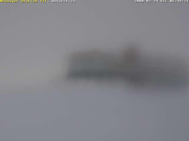 Antarctic research station Neumayer Station III, a long white building with red and blue trim, on the top and bottom, respectively, is elevated on stilts above a snowy landscape.