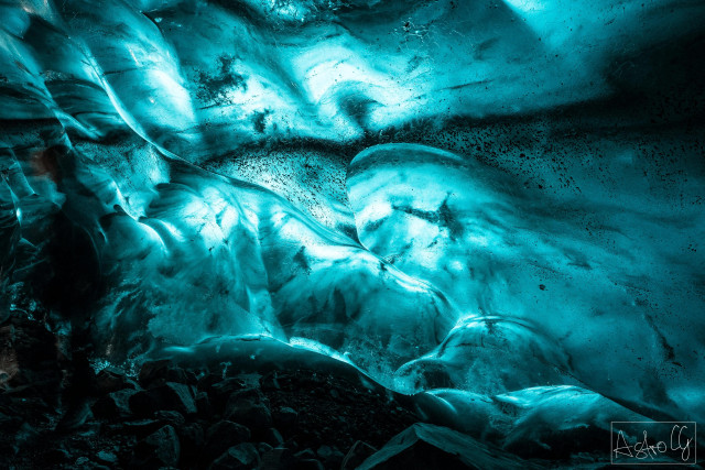 Interior view of an ice or glacier cave with smooth, curved ice surfaces and rocks on the floor