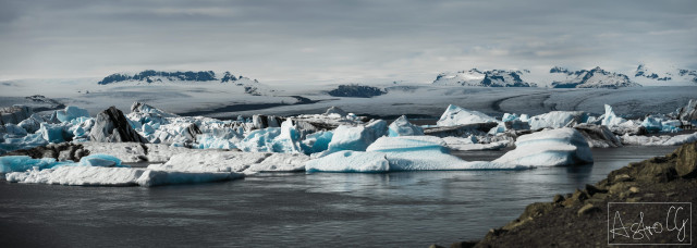 Panoramic view of an arctic landscape with floating icebergs in the water and snow-covered mountains in the background