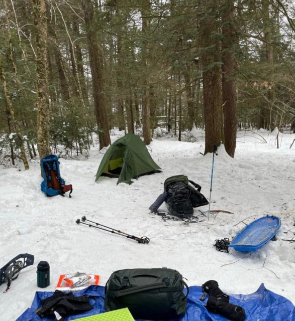 Camp site with a hiking tent in a snow packed clearing in the woods, trees in background.