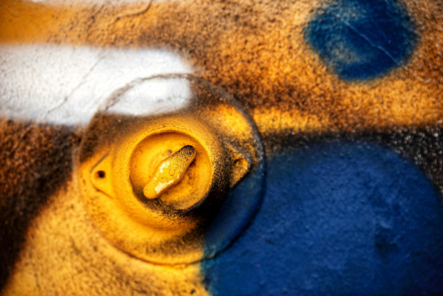 Das Bild zeigt einen alten Drehlichtschalter der an einer mit Graffiti besprühten Wand installiert ist. Er ist fast teilweise orange-gelb mit einigen schwarzen,weißen und blauen Farbtupfern. Rechts unten und oben sind blaue Kreise gesprüht. Links oben ein weißer Strich.