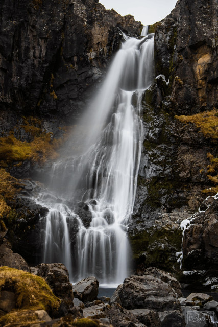 Waterfall cascading over multiple rocky ledges in a rocky terrain partially covered with moss