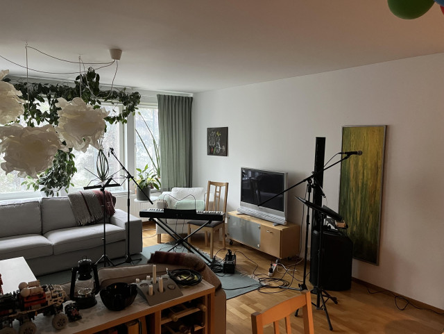 Ett vardagsrum med ett PA, en keyboard och lite mickstativ och notställ.