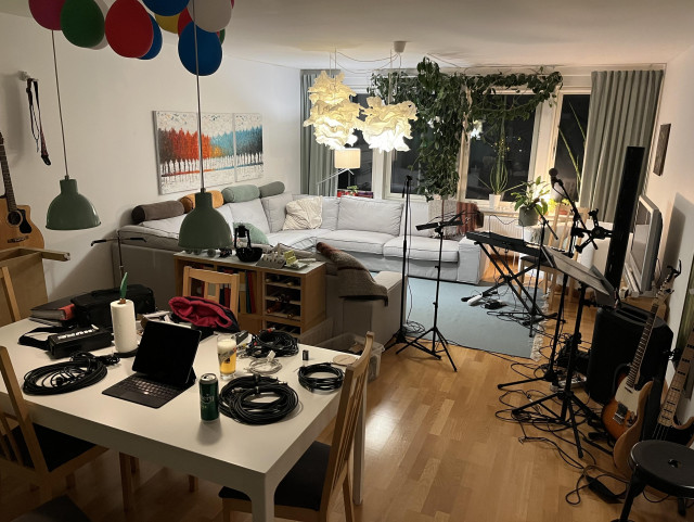 Ett vardagsrum belamrat med musikprylar. Ett matbord med kabelrullar.