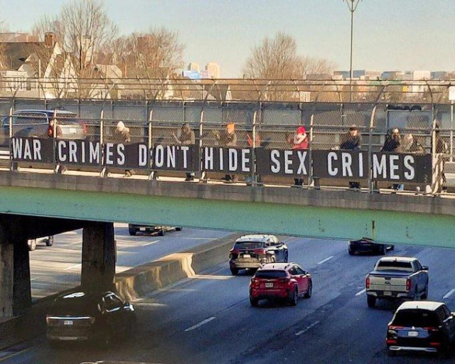 Photo of people holding a banner sign on an overpass that reads: War crimes don't hide sex crimes.
