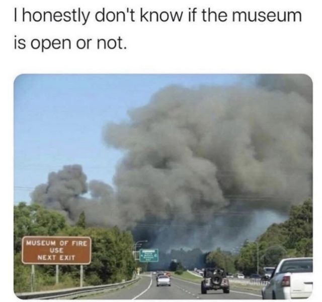 A meme showing a highway with a brown sign that reads "MUSEUM OF FIRE USE NEXT EXIT." In the background, a massive plume of dark grey smoke fills the sky. Text at the top reads, "I honestly don't know if the museum is open or not."