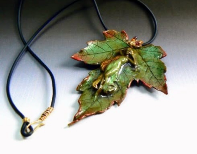 Handcrafted polymer clay maple leaf with warm copper edges, featuring a woodland tree nymph sleeping on the leaf. The nature-inspired necklace has a 14kt bail with sparking garnets and hangs from a black buna cord with hand crafted 14kt clasp. It evokes a quiet forest floor after rain.