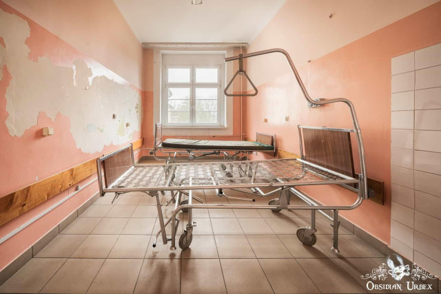 Old hospital ward with pink walls, and old bed sits in the middle foregroud