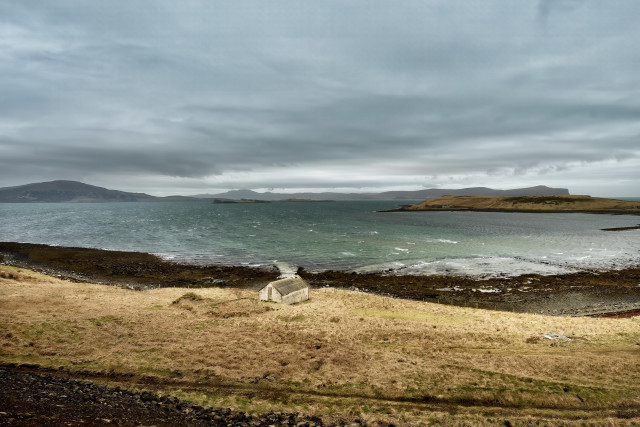 An image of a bay with a cottage on the shore in front.
 And a cloudy sky. Ardmore Bay. Isle of Skye, Scotland