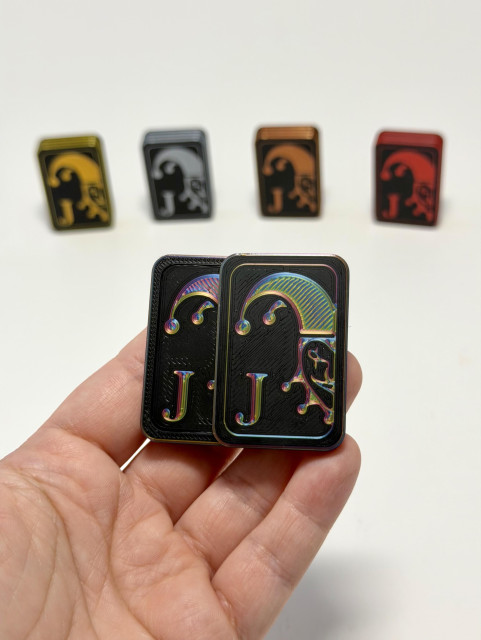 Hand holding a magnetic fidget with a joker face on the front. Printed in shiny silk RGB, with gold, silver, bronze and red variations behind. 

Also available: Ace and King cards. 