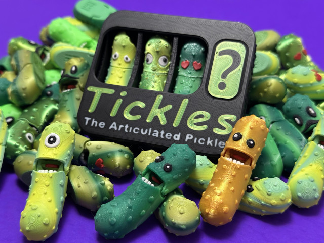 In a purple background: a pile of pickles! They’re articulating mini fidget toys. They come in a variety of faces/expressions and shades of green. I offer mystery packs and pick your own packs. This particular photo is highlighting the golden pickle! Find them and other colour variations in the mystery packs. 