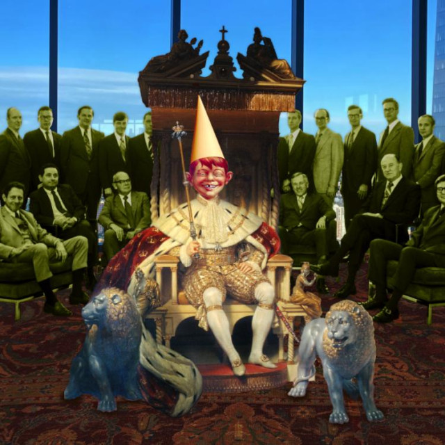 A king on a sumptuous, much elaborated throne; in one hand he holds a sceptre of office, in the other, the leashes for two fierce stone dogs that guard the throne. The king's head has been replaced with a character who was used as the basis for MAD Magazine's Alfred E Neumann. The new head sports a conical dunce cap. Behind the king is a large group of 1960s business men, seated and standing, in conservative suits. The background is the view from the 80th floor of World Trade Center 3. The floor has been carpeted in sumptuous tabriz from the Ottoman court.


Image:
Aude (modified)
https://commons.wikimedia.org/wiki/File:80th_floor_of_3_World_Trade_Center_-_OHNY.jpg

CC BY 4.0
https://creativecommons.org/licenses/by/4.0/deed.en
