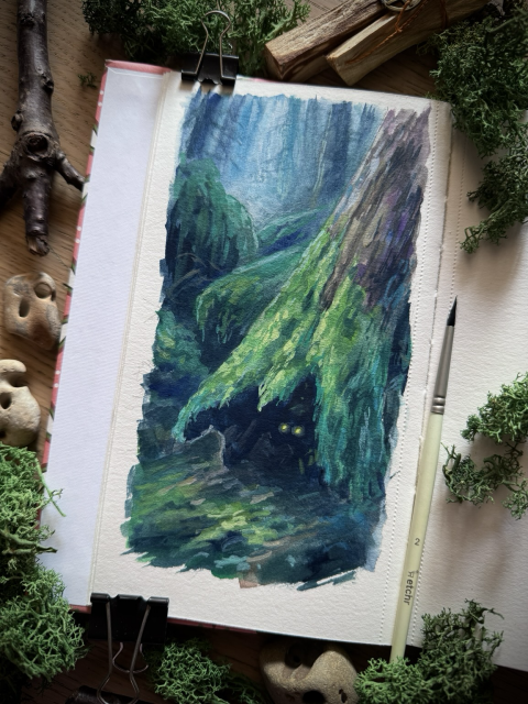 A photo of an open sketchbook, placed on a wooden desk and surrounded by branches, hag stones, moss, and a paint brush. The sketchbook page features a reimagining of the tree from the photo. It is now placed in a gloomy, misty forest, mossy rocks rising behind it. Glowing eyes are visible in the deep shadows inside the tree.