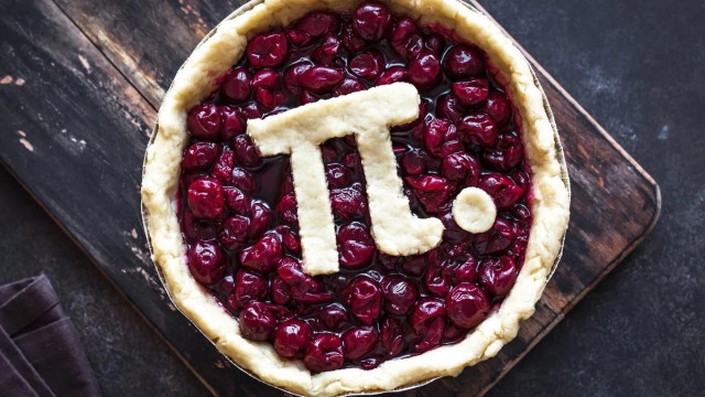 A top-down view of a cherry pie on a dark wooden surface, with a golden crust and the mathematical pi symbol plus a dot cut from pastry and placed on top of the glossy red cherry filling. Image from Hugo Aitken on Unsplash