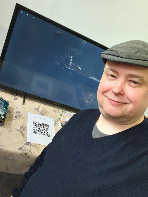 Ein freundlicher Herr mit Mütze vor einem Stand mit Monitor, auf dem ein U-Boot zu sehen ist.