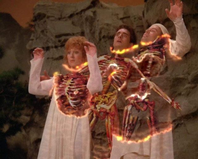 Star Trek The Next Generation scene. Ok so basically what we have here is an outdoor shot with a rock wall cliffy looking background. There are three people, humans, standing together. Their hands are up and raised as if they're going over the drop of a roller coaster, but in actuality, they are in this moment sort of disintegrating. You can see their faces and arms and lower half, dressed in while linen, but the midsection of each person is sort exploding and disappearing and on fire. Layers are removed, so you see bones and some organs and I imagine if you kept watching this disintegration would work its way outward and a second later they'd basically be toast. No caption, just a fun and happy light hearted Saturday Star Trek post!