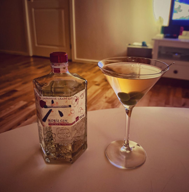 A photo of a dirty dry martini with 3 olives next to a bottle of gin.