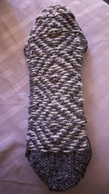 a sock knit in two shades of grey with a dark toe and a stranded diamond pattern for the rest, turned inside out so the floats (unknit yarn behind knit stitches of contrasting colours)