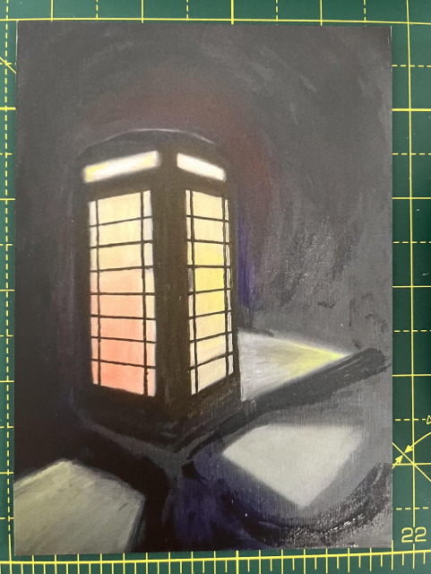 Telephone box, dark background, lights are on and the light is shining on the pavement at the side.