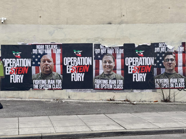 Street posters wheat-pasted on a wall in Washington, D.C., showing three repeated poster designs featuring portraits of U.S. military service members in uniform against an American flag background. Each poster reads “OPERATION EPSTEIN FURY” and “FIGHTING IRAN FOR THE EPSTEIN CLASS.” Individual posters name “Noah Tietjens did not have to die” and “Nicole Amor did not have to die,” with a third partially visible. 