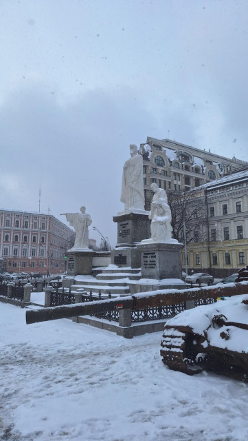 Three statues overlooking the vehicular wasteland of the wreckage of war in a snow covered square in Kyiv.