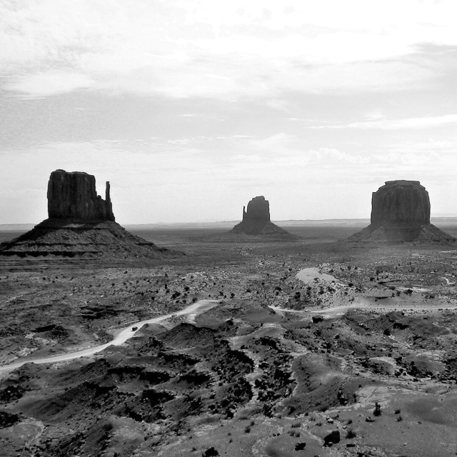Drei bekannte Felsen in Arizona, USA. Ansonsten flaches, fast unwirtliches Land gegen hellen Himmel, s/w. 