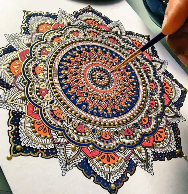 Photo of a close up of a neatly created intrcatei mandala arwork in orange gold blue and black.
