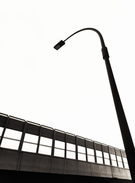 Silhouette of a tall street light over a very uniform row of windows set in concrete.