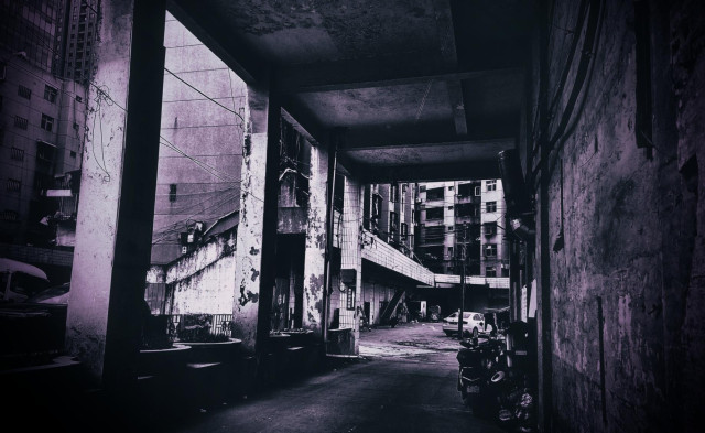 Corroded and shadowy concrete structure with pillars leading to an older building.
