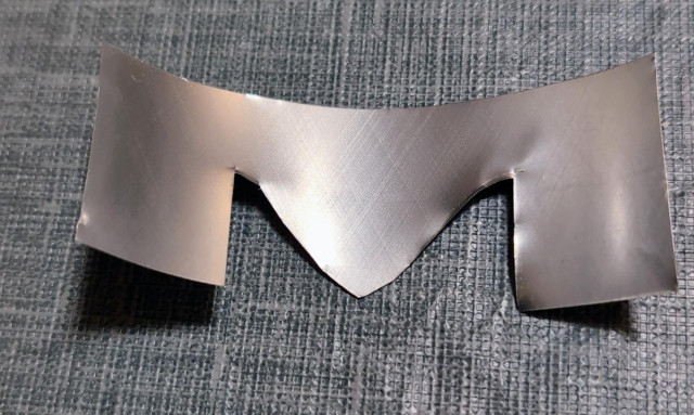 A 2.5" by 1" rectangular piece of soda can, cut into the shape of the letter "M".