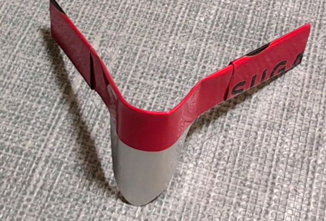 The final soda can padlock shim, with the legs of the "M" shape folded up and over, and the whole shim rounded out to fit around a padlock shackle.